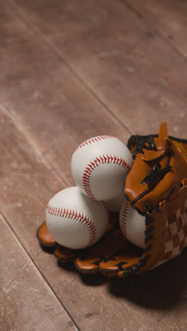 Vídeo-Vertical-De-Cerca-Estudio-De-Béisbol-Bodegón-Con-Pelotas-Y-Guantes-De-Receptor-En-El-Suelo-De-Madera